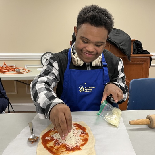 Cooking class student putting cheese on pizza